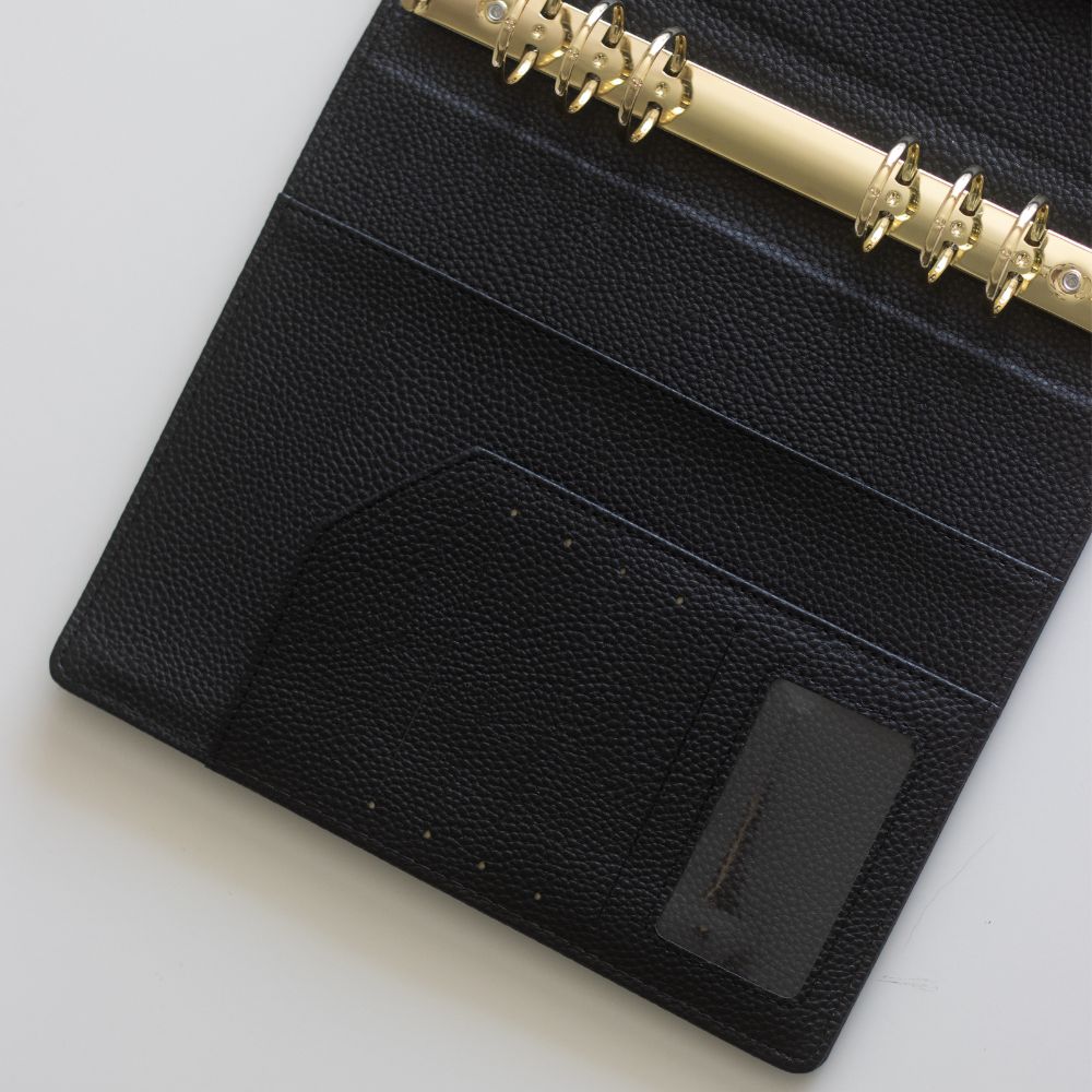 Pockets on a black textured vegan leather ringbinder cover with six gold rings on a light grey background