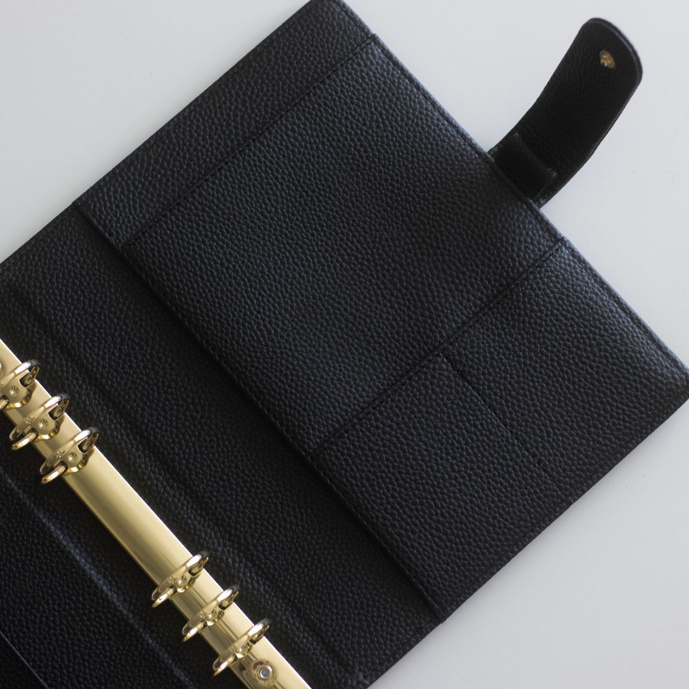Black vegan leather ringbinder with six gold rings on a white background