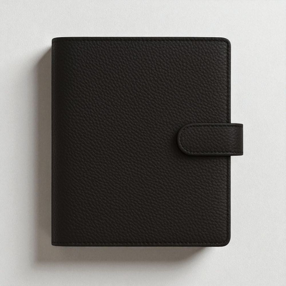 Black faux leather A5 ringbinder with six gold rings on a light grey background