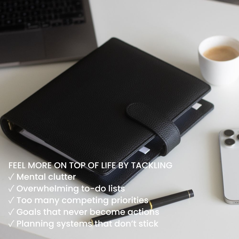 Black A5 vegan leather planner on a desk with a pen, smartphone, and coffee cup.
