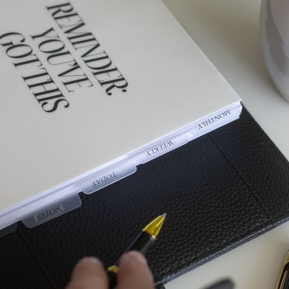 Black ringbinder planner with motivational quote and pen on a light surface