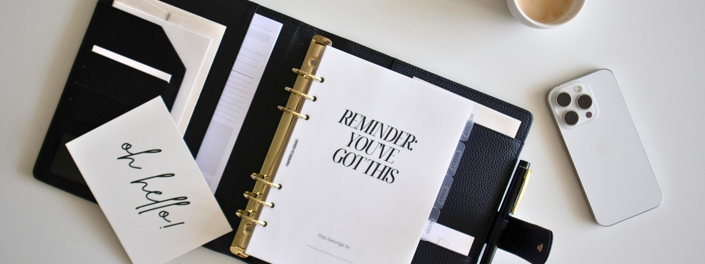 Open ringbinder planner with a message on a desk with a phone and coffee cup.