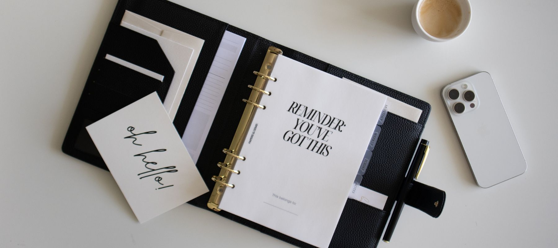 Black ringbinder planner with motivational quote, coffee cup, and phone on a light surface